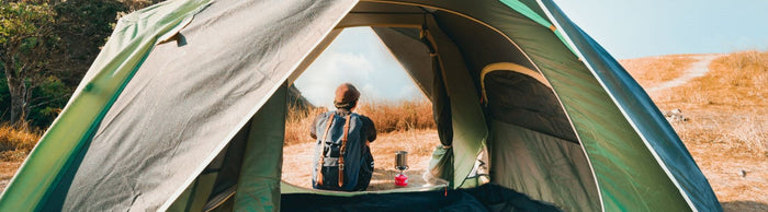 a man sitting in front of a tent looking out on a landscape, photo taken through opening of a tent