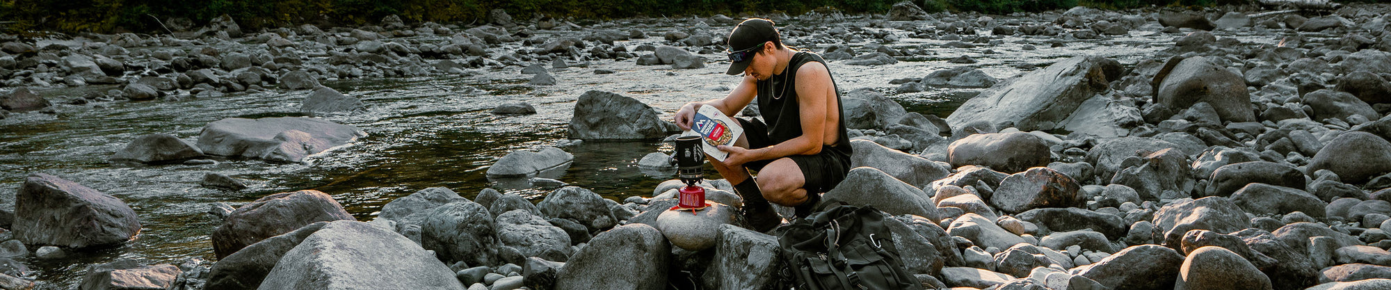 Backcountry hiker preparing a Mountain House pouch by a creek